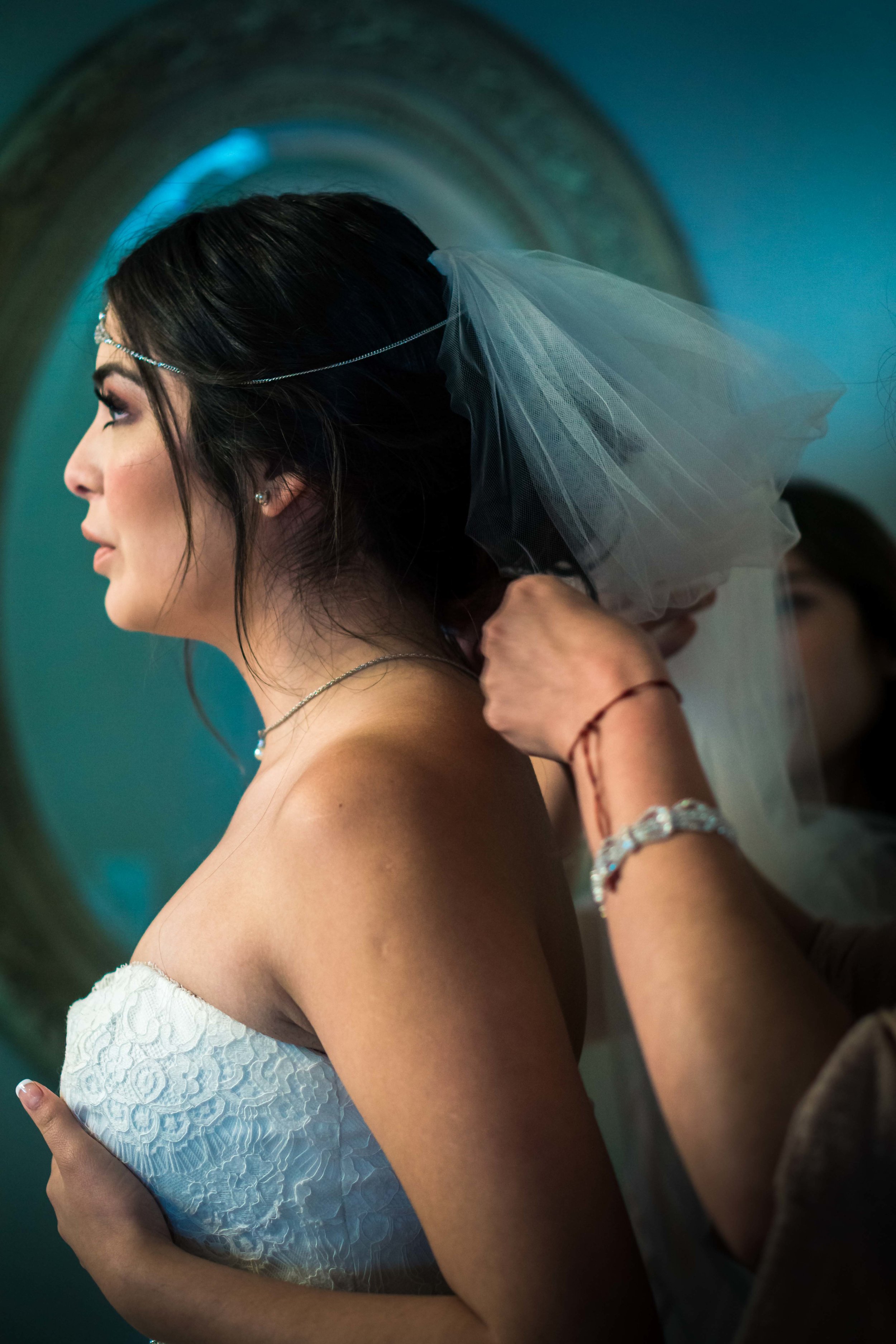 Photo of the stunningly beautiful bride with a blue reflection With her mom and sister helping her put her veil before the wedding On Balboa Island