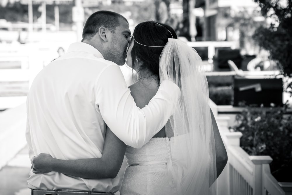 Black-and-white candid photo of the bride and groom kissing and walking together