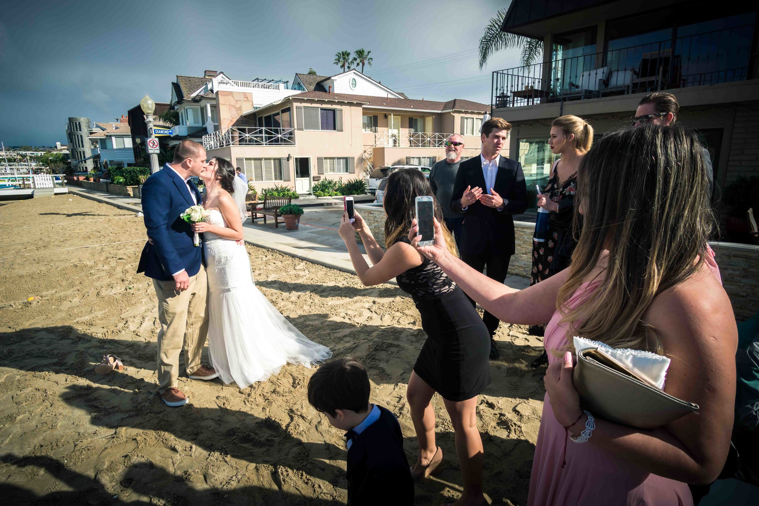 Wedding guests taking photos of bride and groom kissing