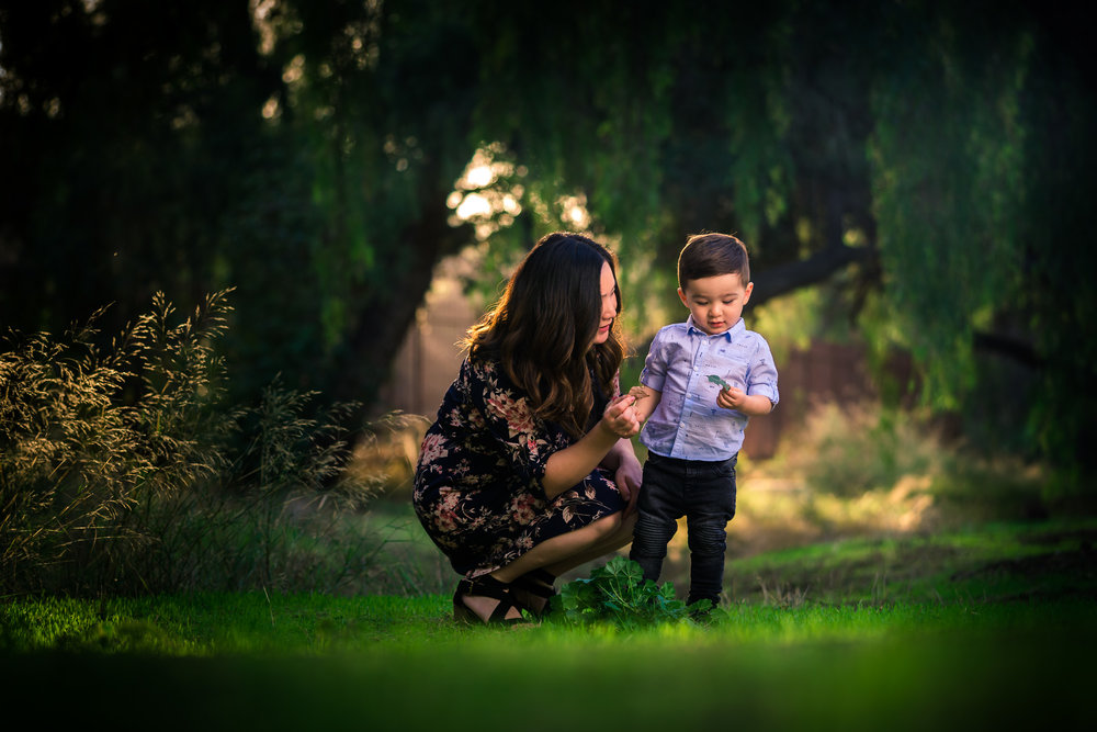 Candid photo of a little boy and mother during a Family portrait photo shoot in Fullerton on the Juanita Cooke greenbelt and Trail with vibrant green trees and grass and the golden hour sun