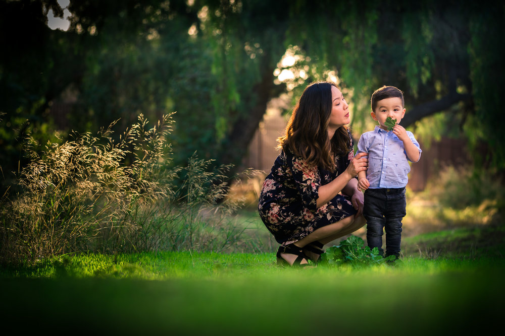 Candid photo of a little boy playing with mother during a Family portrait photo shoot in Fullerton on the Juanita Cooke greenbelt and Trail with vibrant green trees and grass and the golden hour sun