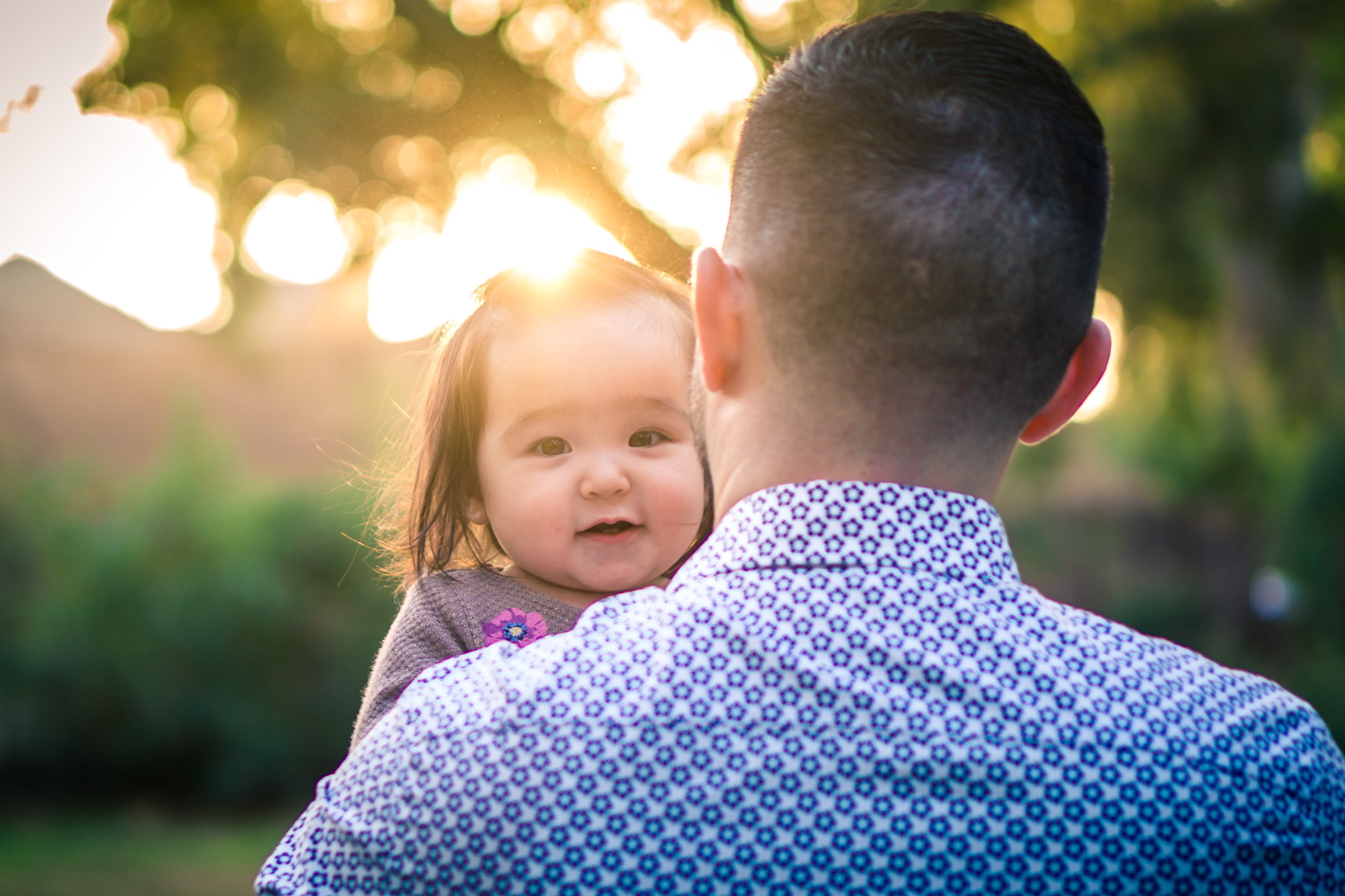 Portrait of a cute little baby girl looking back on her fathers shoulders during a family portrait session in fullerton orange county taken by joseph barber photography