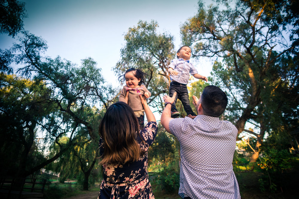 photo of a mother and father tossing up their little children during a family portrait session  on the juanita cooke trail in fullerton orange county taken by joseph barber photography