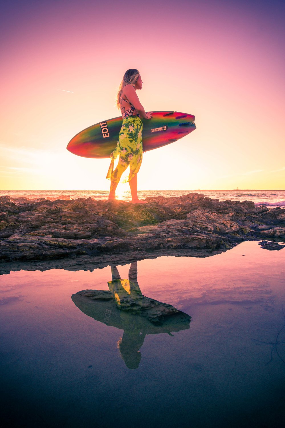 ​​​​​​​Surfer girl portrait at little corona beach with her reflection mirrored in the glassy tide pools at sunset