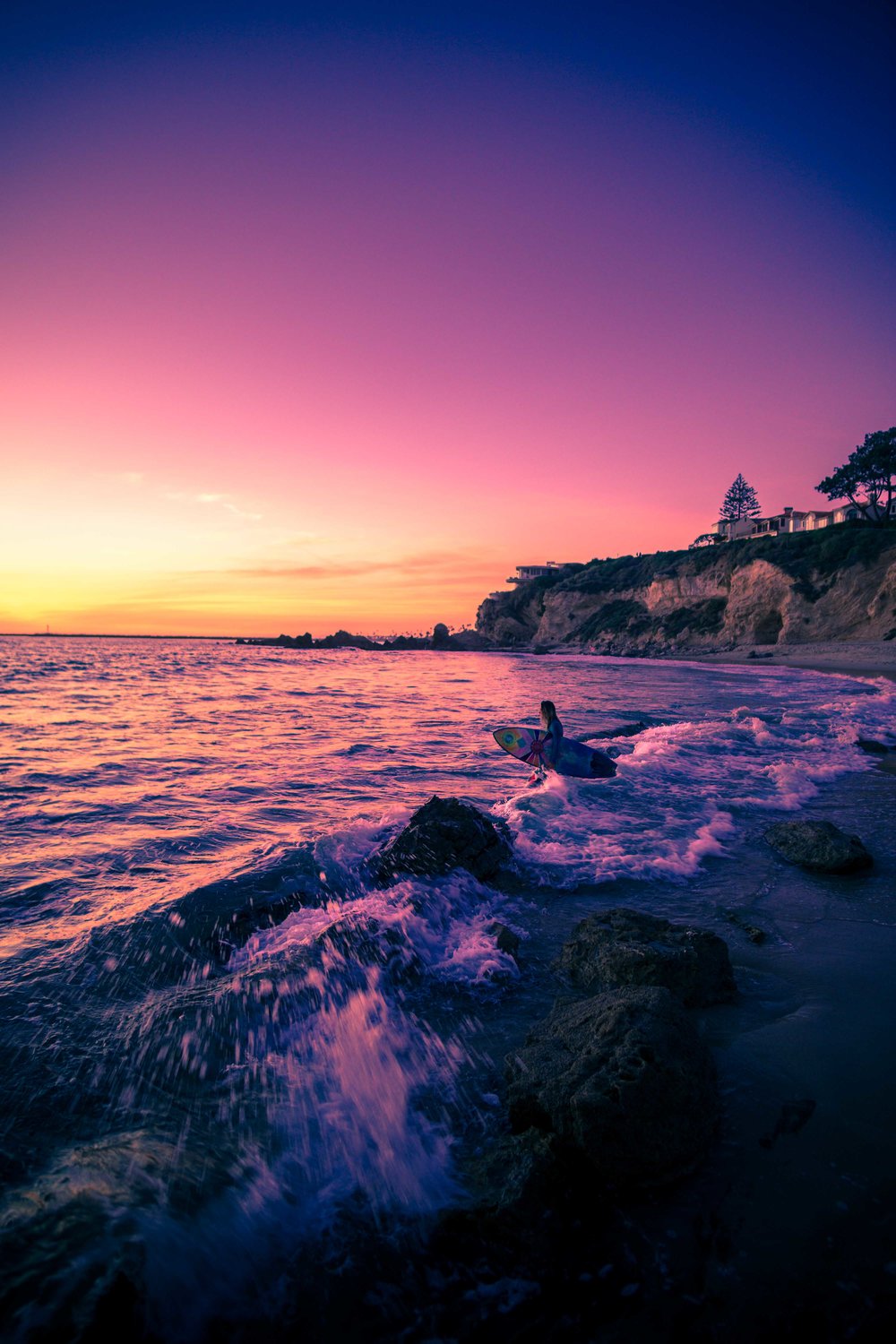 Wide angle photo of a surfer girl walking out to the waves at Corona Del Mar beach during Sunset