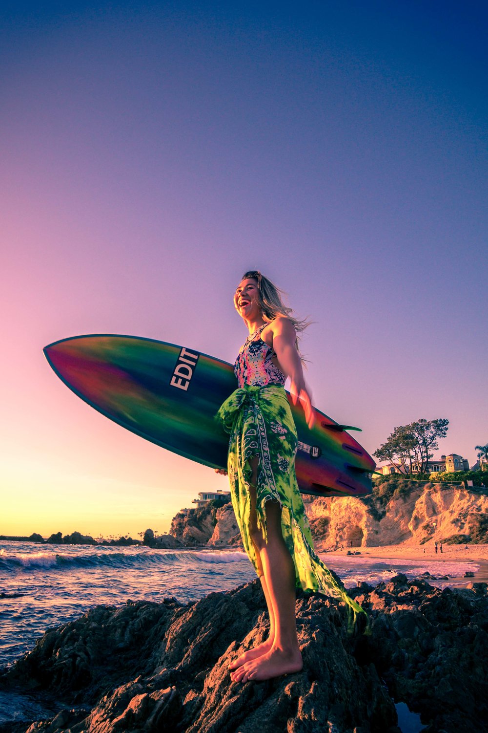 Portrait of a surfer girl with her vibrant attire and hand painted surfboard at the little corona beach