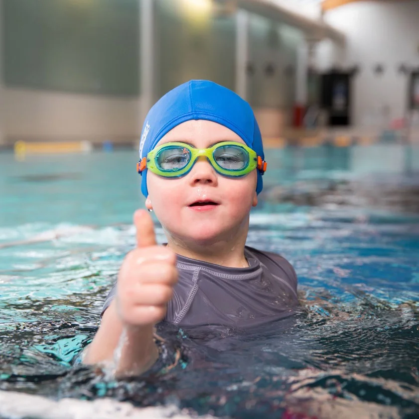 Preschool boy gives a big thumbs up in the pool.