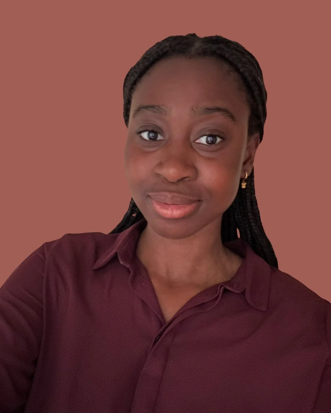 A young woman with braided hair, wearing a maroon shirt and earrings, smiling at the camera against a brown background.