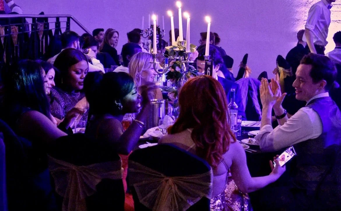 People sitting at a formal dinner table with candles and floral centerpieces, enjoying conversation and celebration.