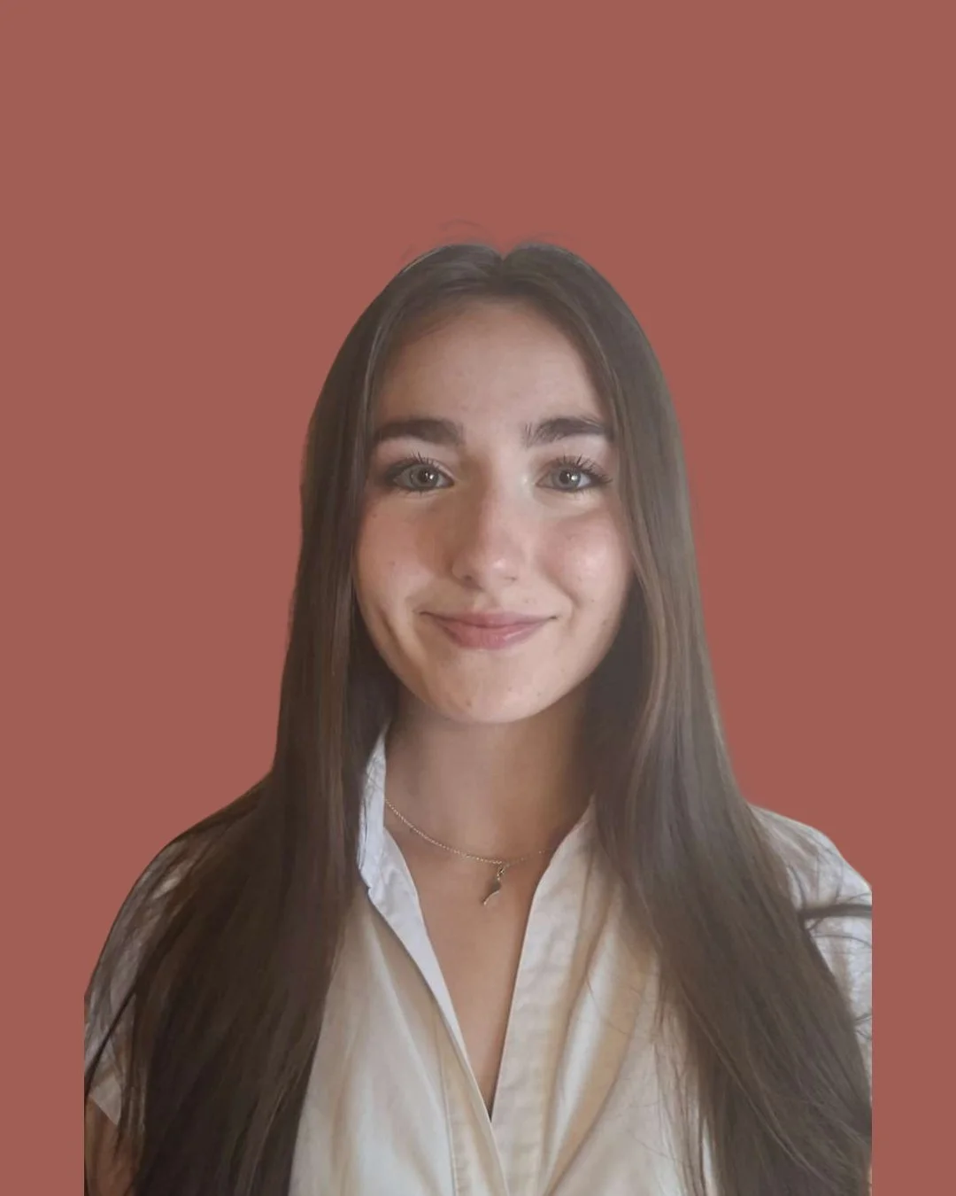 A young woman with long brown hair smiling at the camera, wearing a white blouse and a delicate necklace, against a plain, muted brown background.