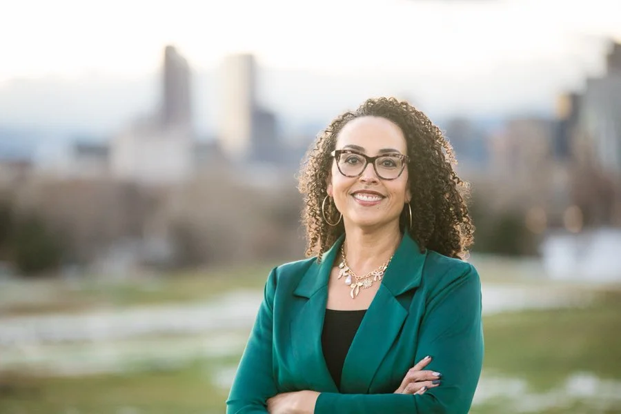 Cherri McKinney in a green suit outside with Denver skyline in background