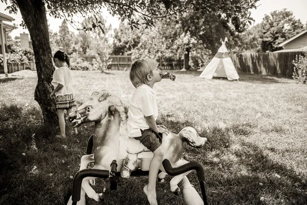 Kids playing in the yard with a plastic horse on springs and a teepee in the background.