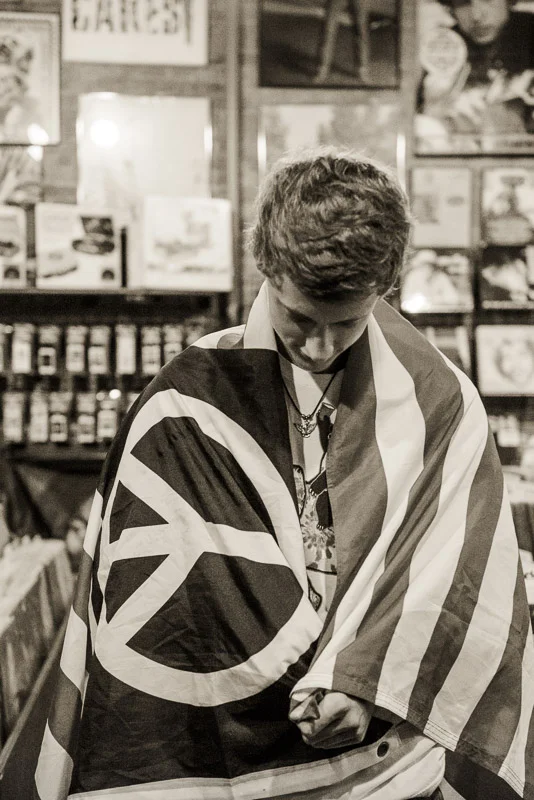 high school senior boy in record store wrapped in a peace sign flag