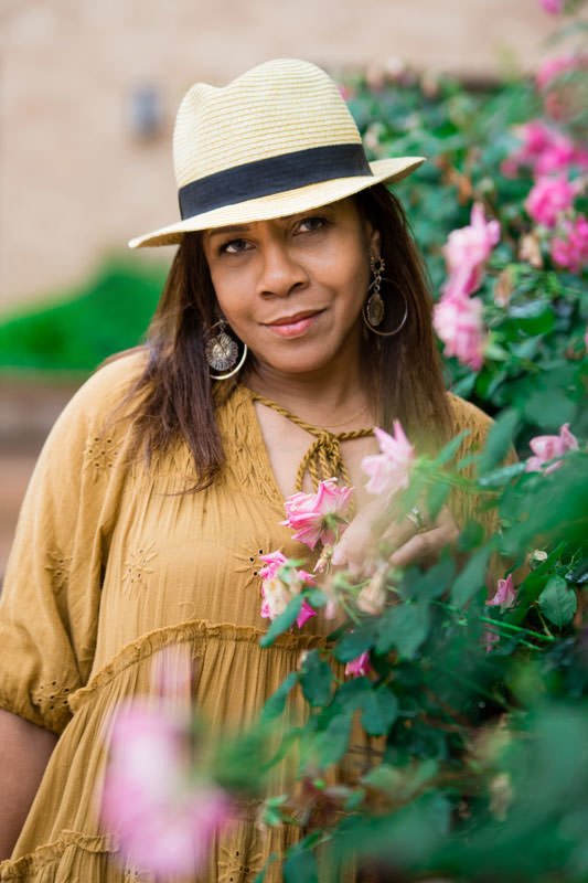 Portrait of author Charita "rita" Cauthen wearing white hat and mustard yellow dress in a garden at Kent Place Apartments 