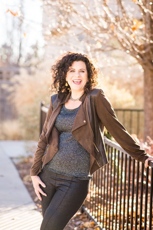Dr. Elizabeth Yarnell autoimunity nutrition and health speaker and author outdoors in the fall wearing a leather jacket with her curly hair blowing in the wind