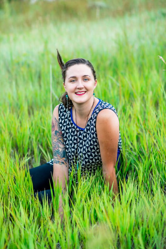 UX designer Lexi Doig Steele in sleeveless shirt sitting in grass with a feather in her hair.