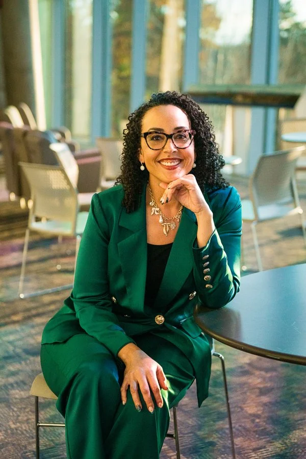 woman in a green suit sitting at a table smiling