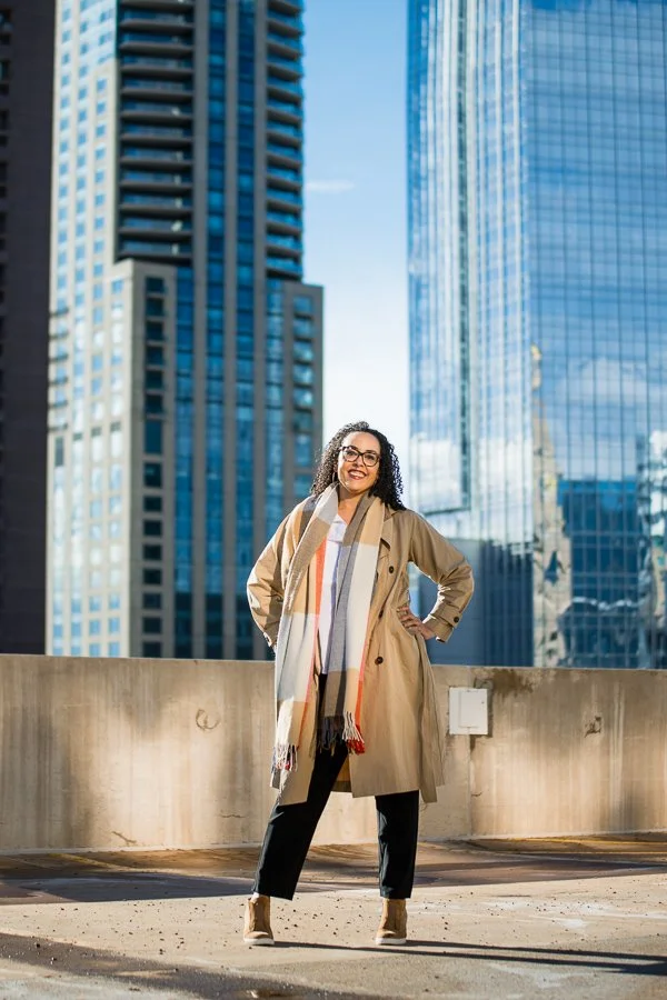 Cherri McKinney outdoors in a raincoat and scart with highrise buildings in the background
