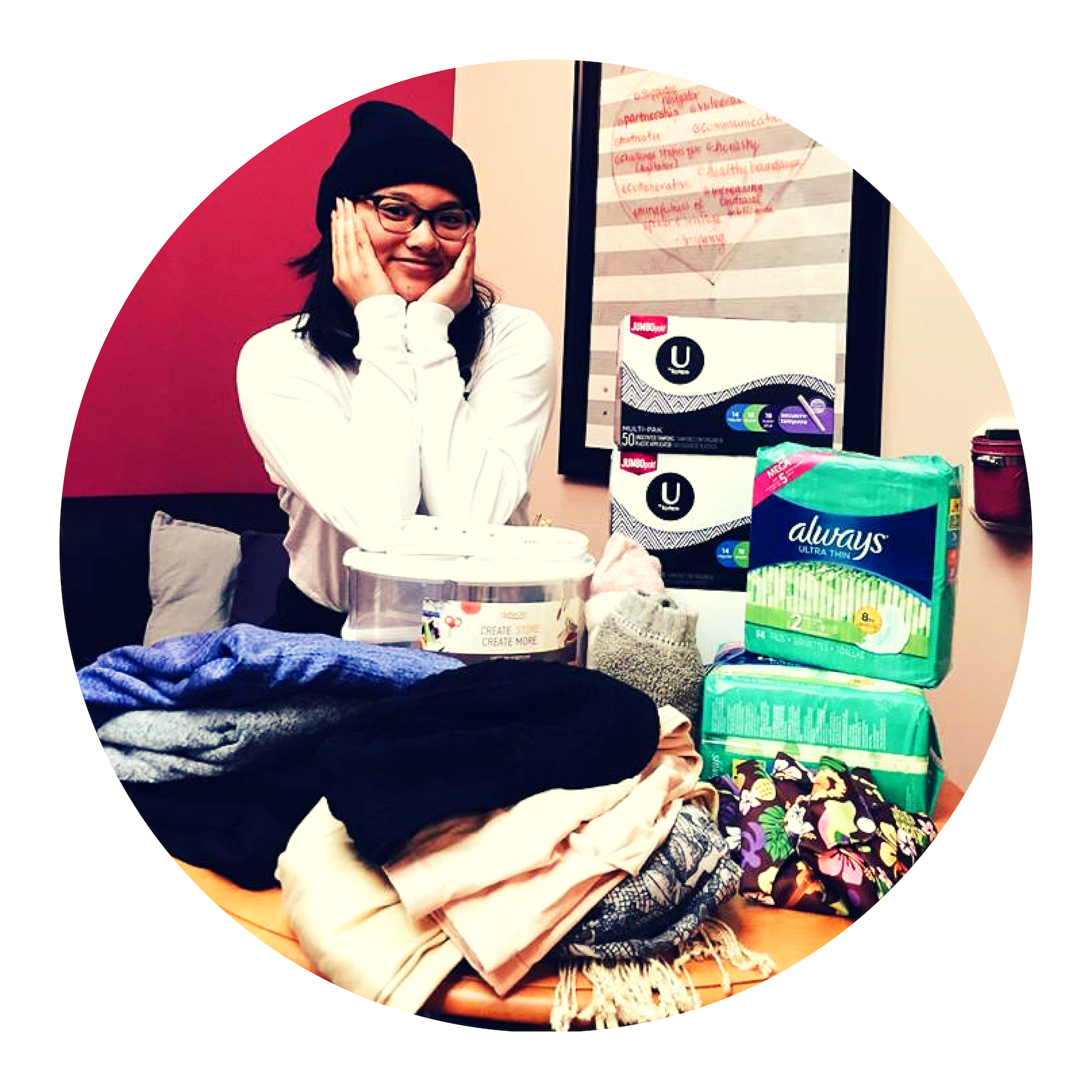A staff member smiling above a recent box of donations of menstruation pads, tampons, clothing, and more!