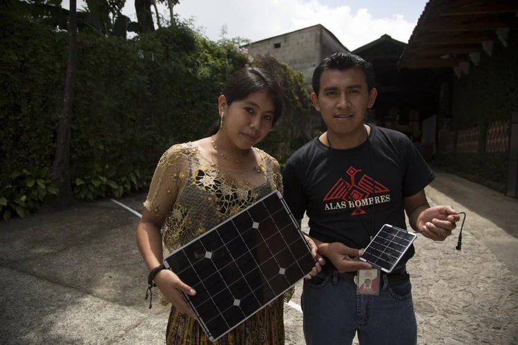 Two community members hold portable solar panels from a charging kit.