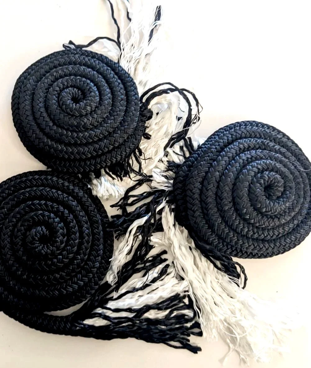 Three coiled black woven textile pieces, the early stages of a rope piece. 
