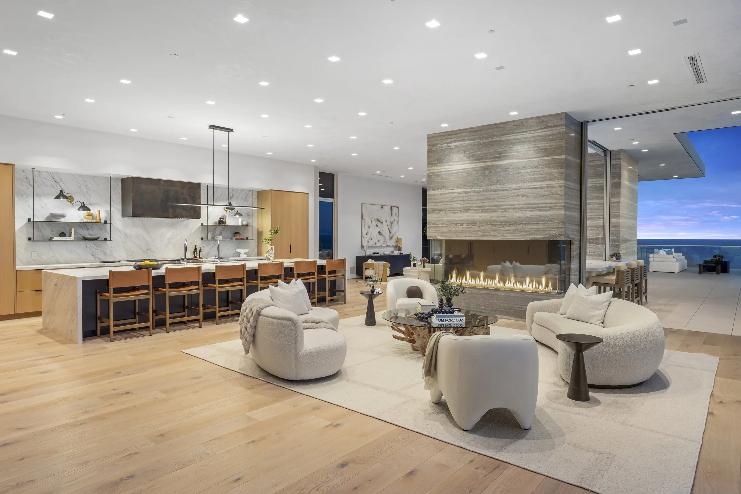 Modern open-concept living space with a kitchen island, white leather furniture, a fireplace, and ocean view
