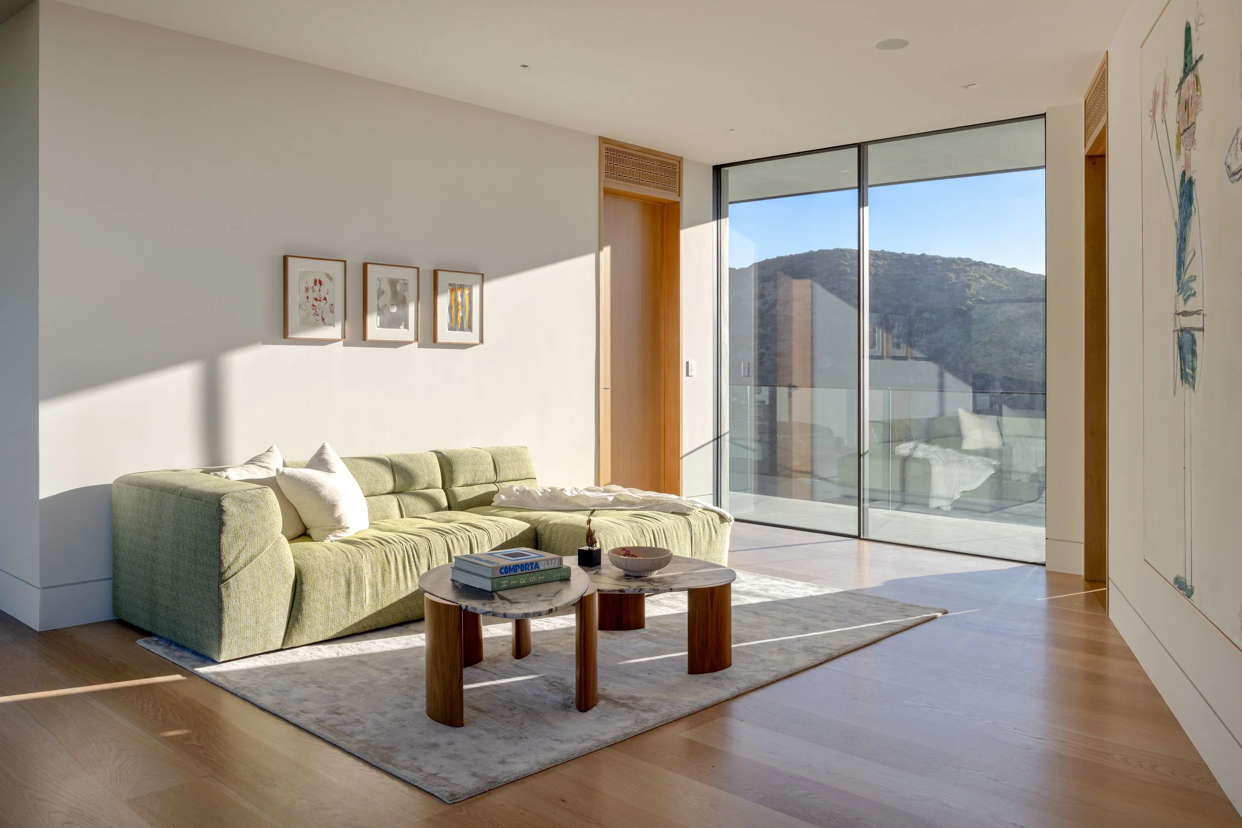 Modern living room with green sofa, wooden coffee table, large glass sliding doors, and mountain view.