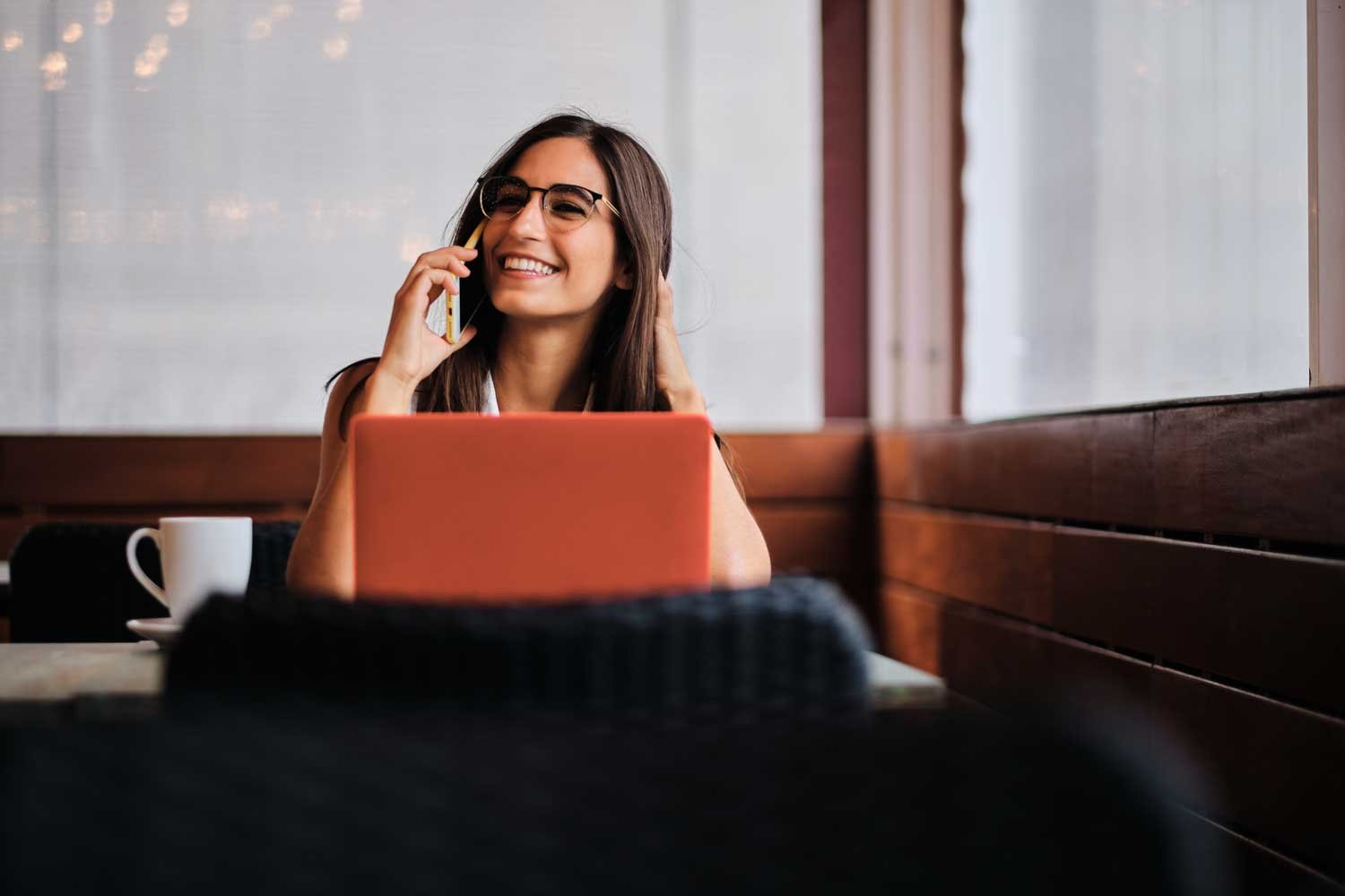 cheerful young woman talking to the mobile while working on a laptop