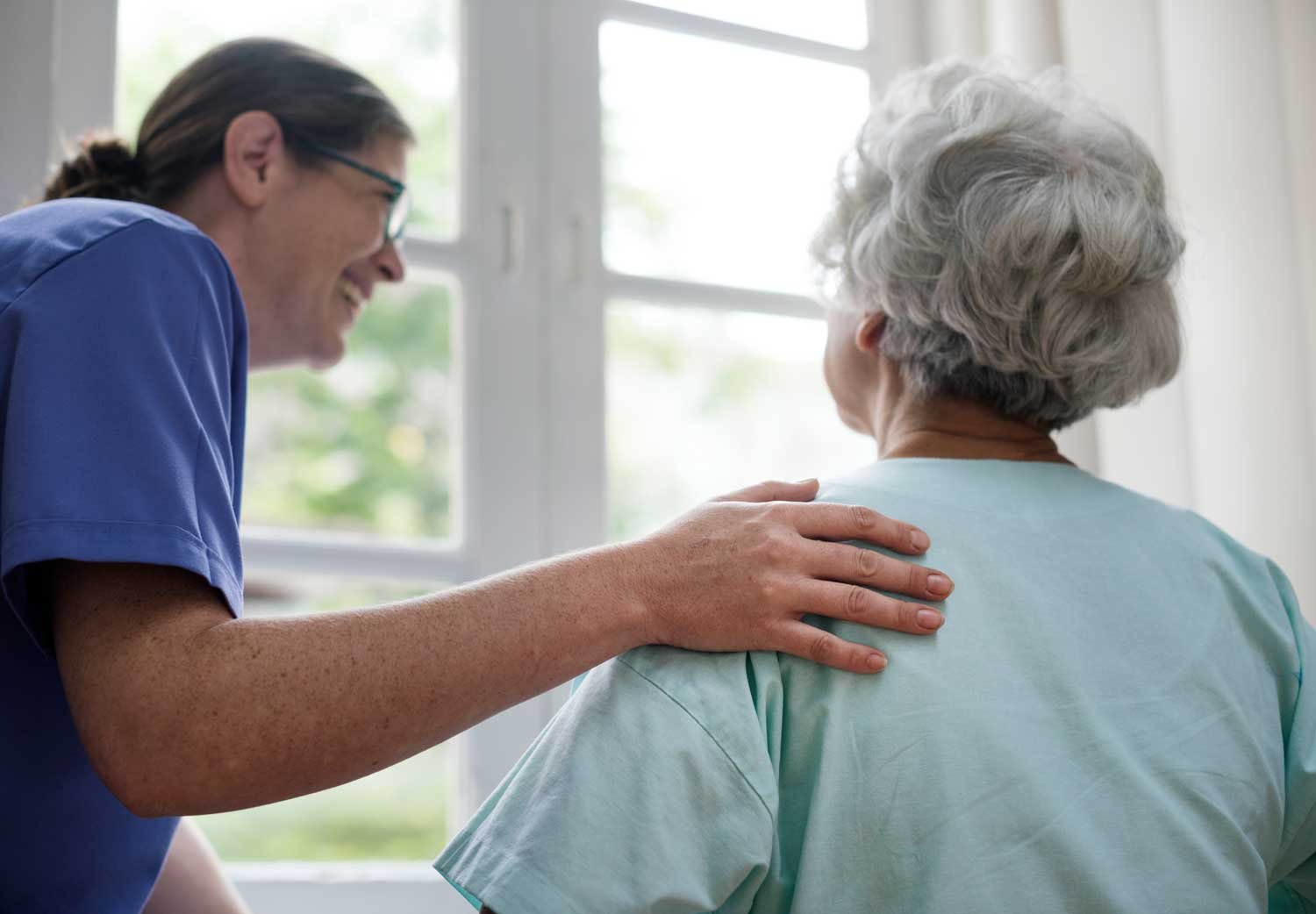 nurse looking after an elderly woman, she's holding her hand on her shoulder and smiling