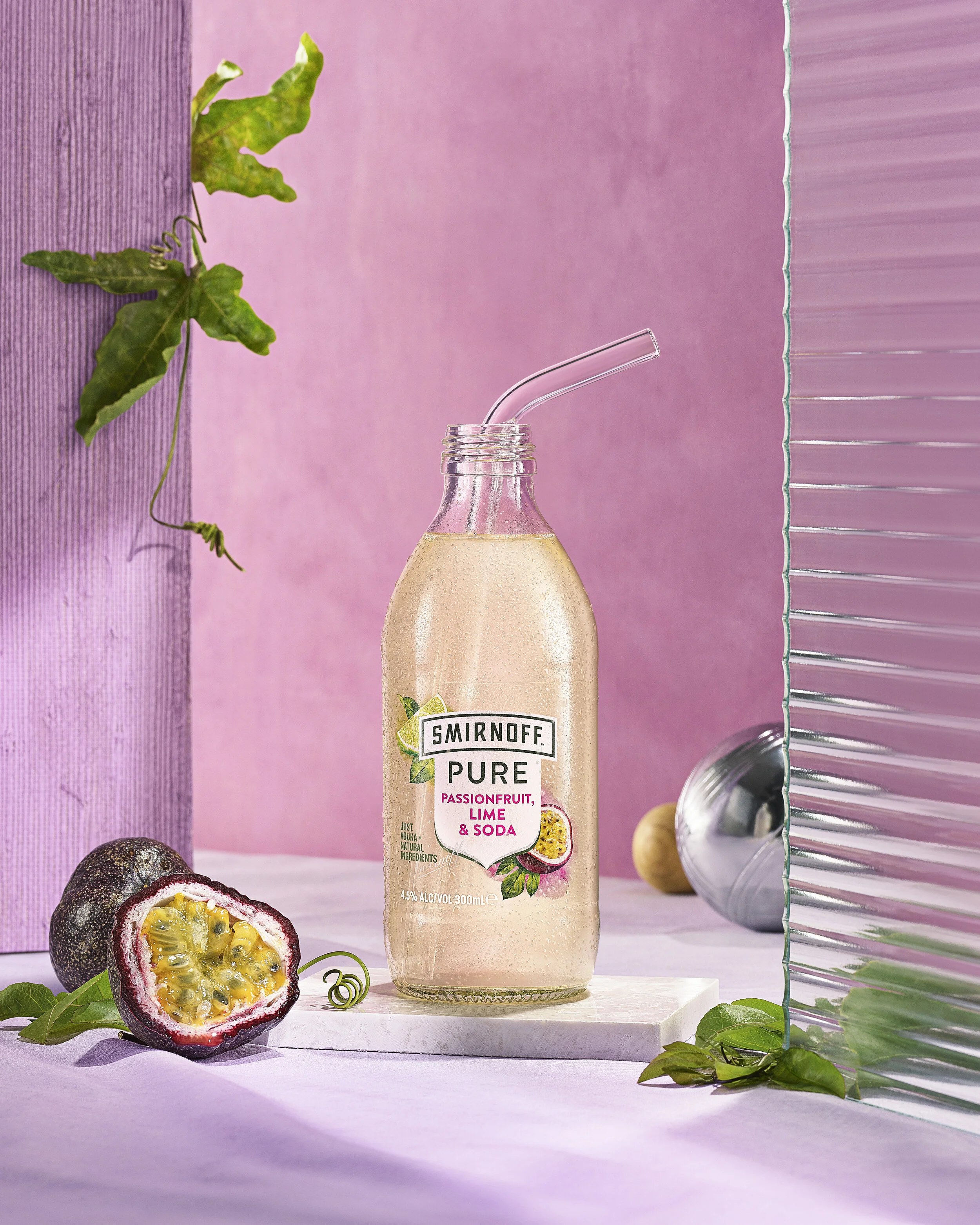  Advertising image for Smirnoff Pure Passionfruit Lime and Soda, sitting on pink and purtple set and fluted glass with bocce set and passionfruit. Advertising beverage photographer. 