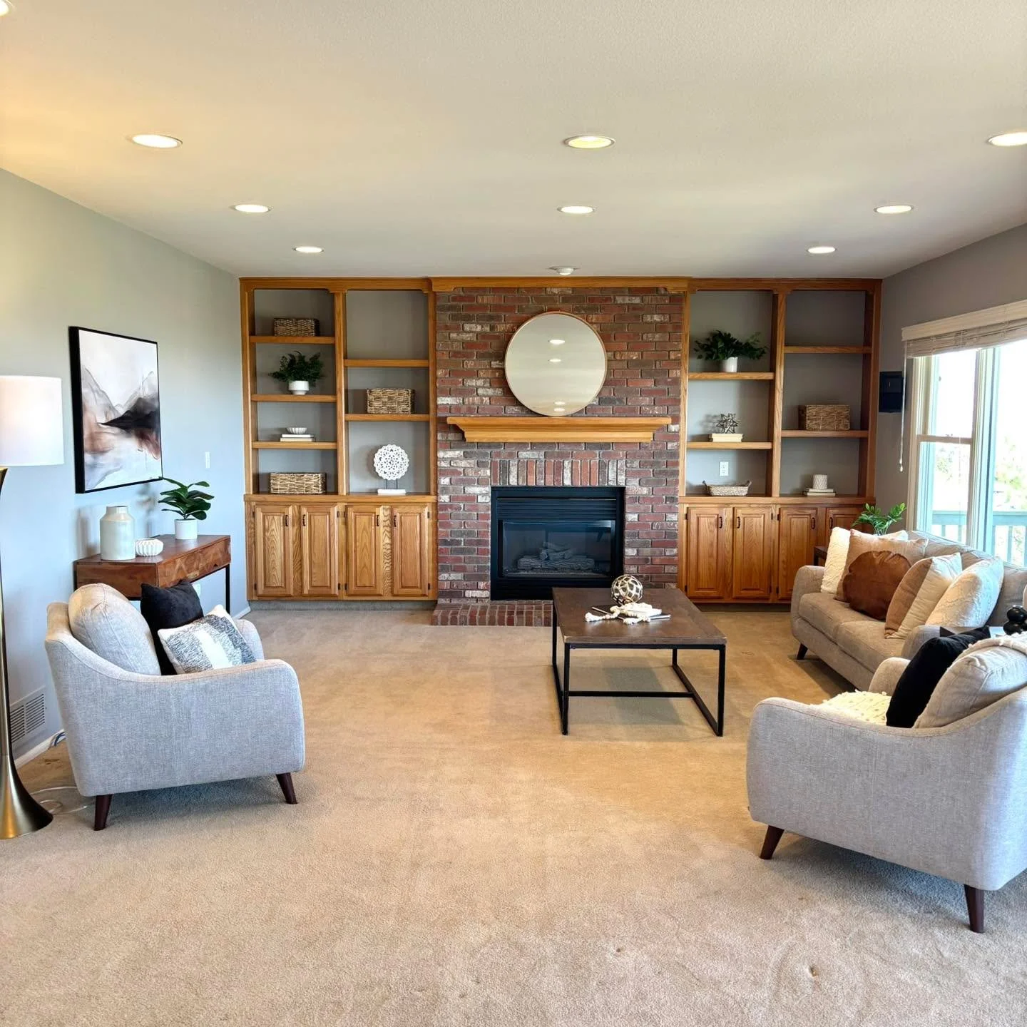 Clean lines, cozy textures, and a statement focal point that anchors the entire space ✨ This beautifully staged living room highlights a classic brick fireplace framed by custom built-ins, creating both warmth and function. Soft neutral seating invit