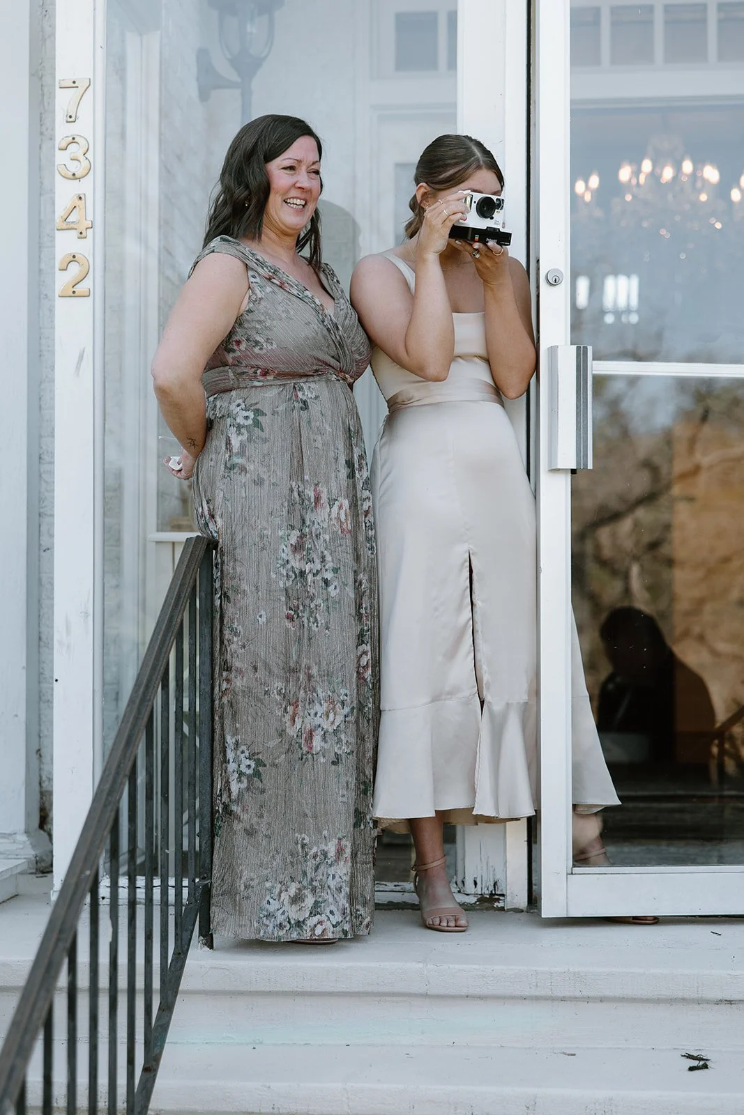 Two women standing in a doorway, one with a camera, capturing a joyful moment.