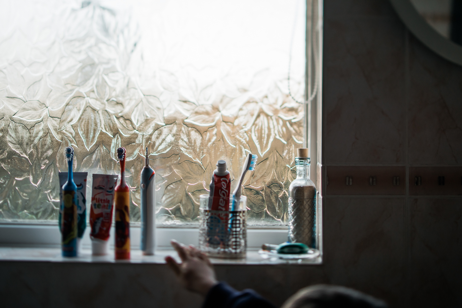 child's hand reaching for toothbrush on bathroom windowsill