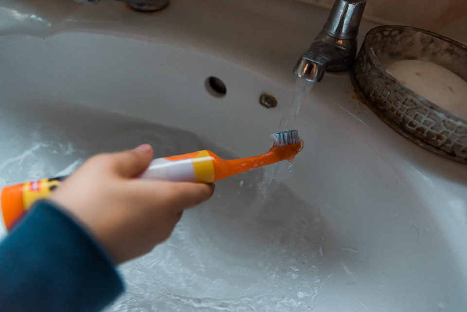 Child washing his orange toothbrush under tap during bedtime rou