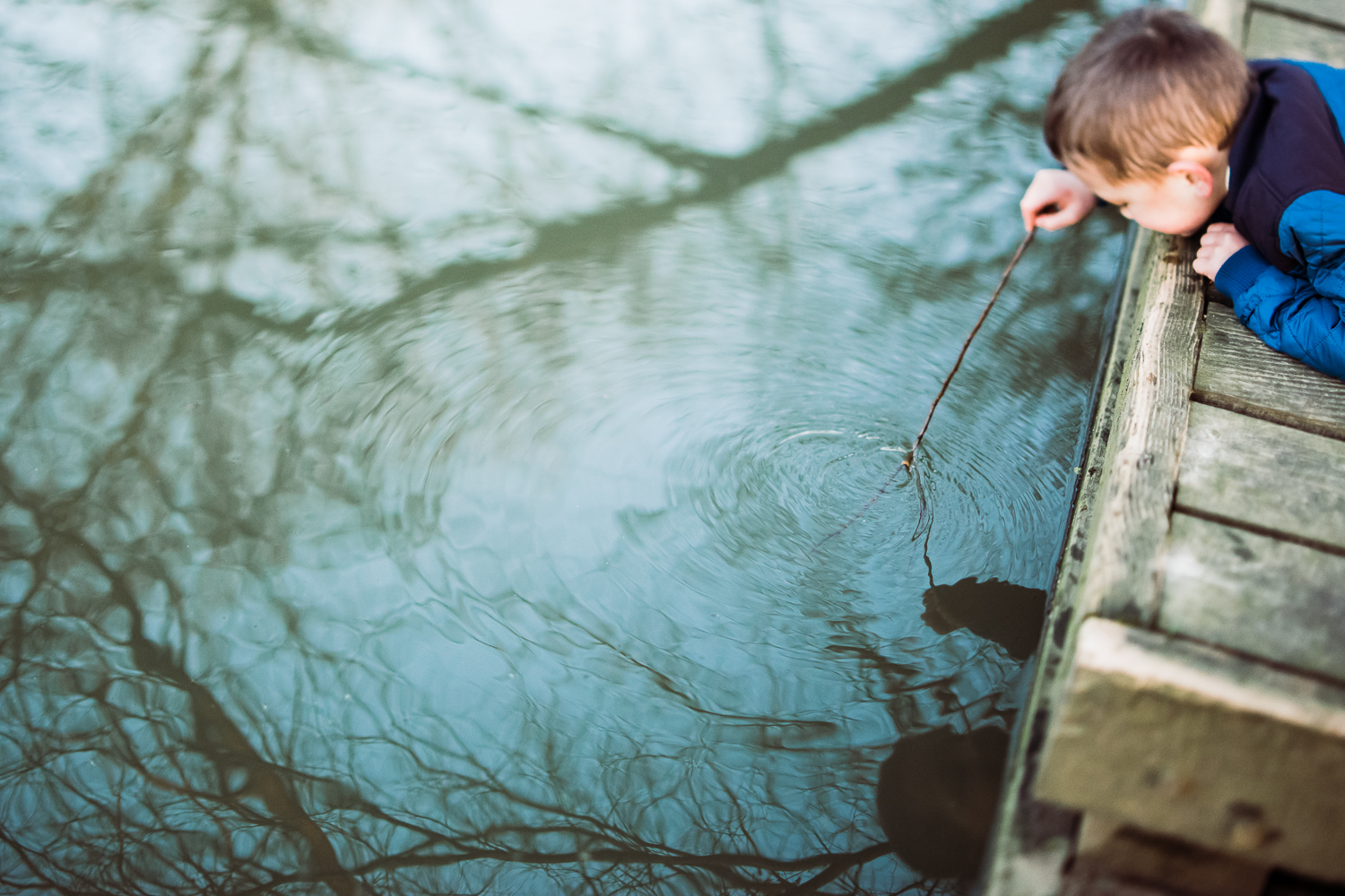 Boy dipping a stick into the water creating ripples