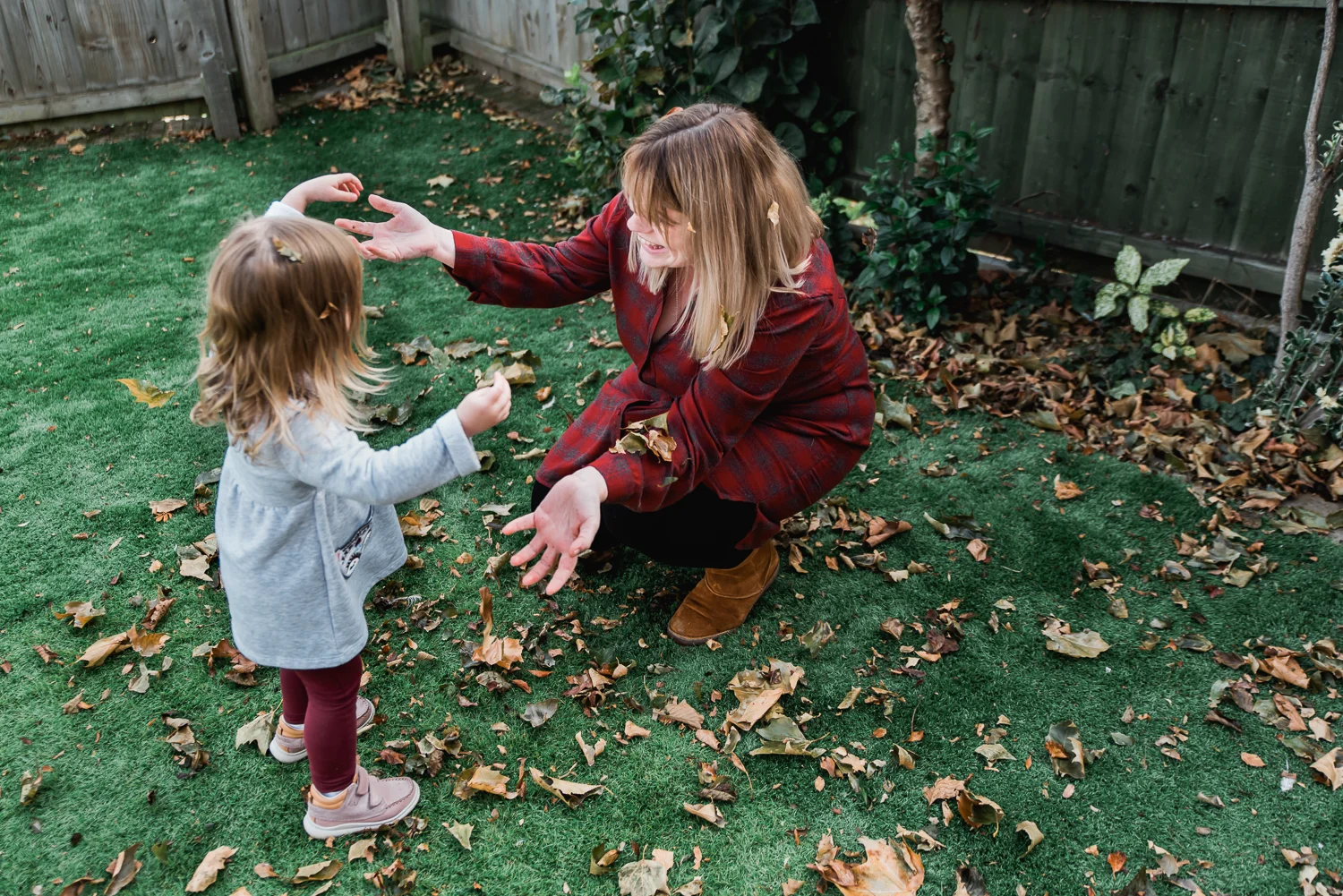 Mum and daughter dressed in red playing with the brown leaves in