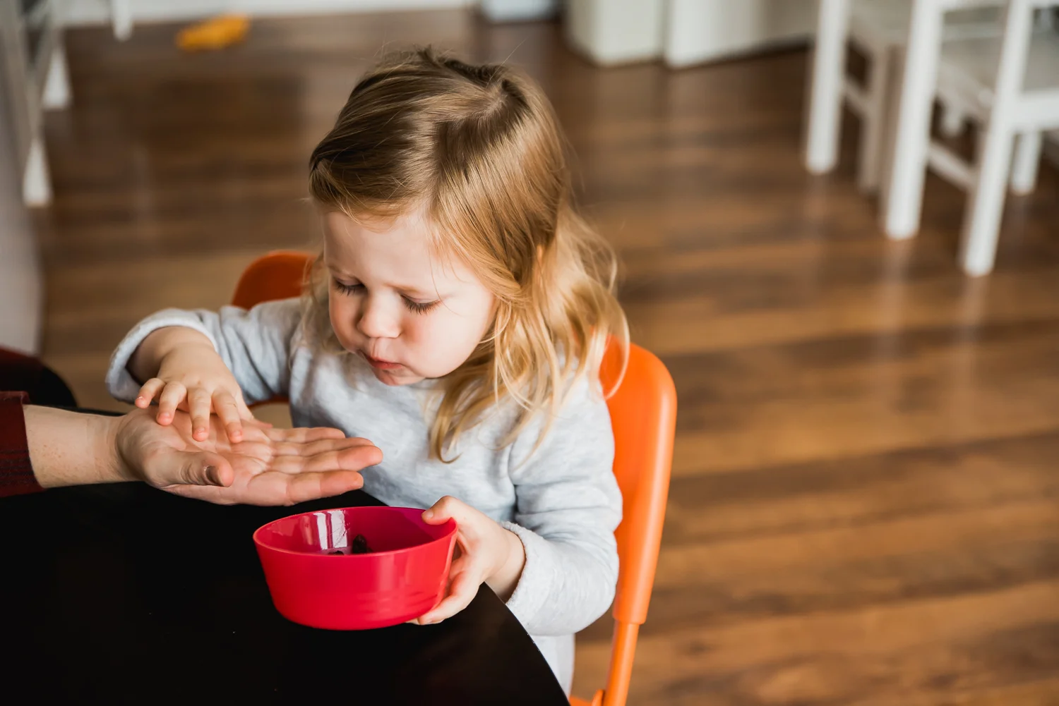 Child handing raisin to her mum's hand from her red bowl