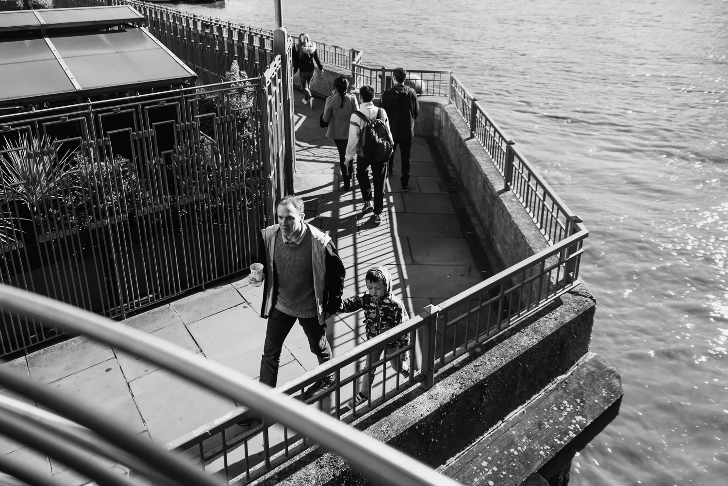 Black and white photograph of a father and son walking by the ri