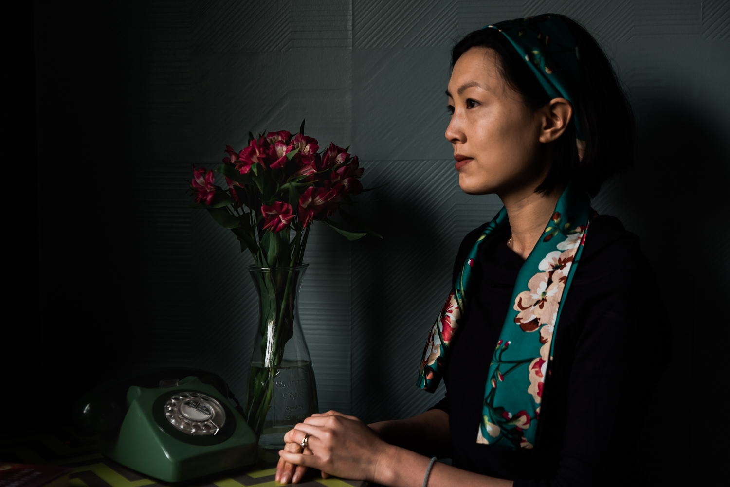 Photographer sits with a vase of pink flowers and a telephone at