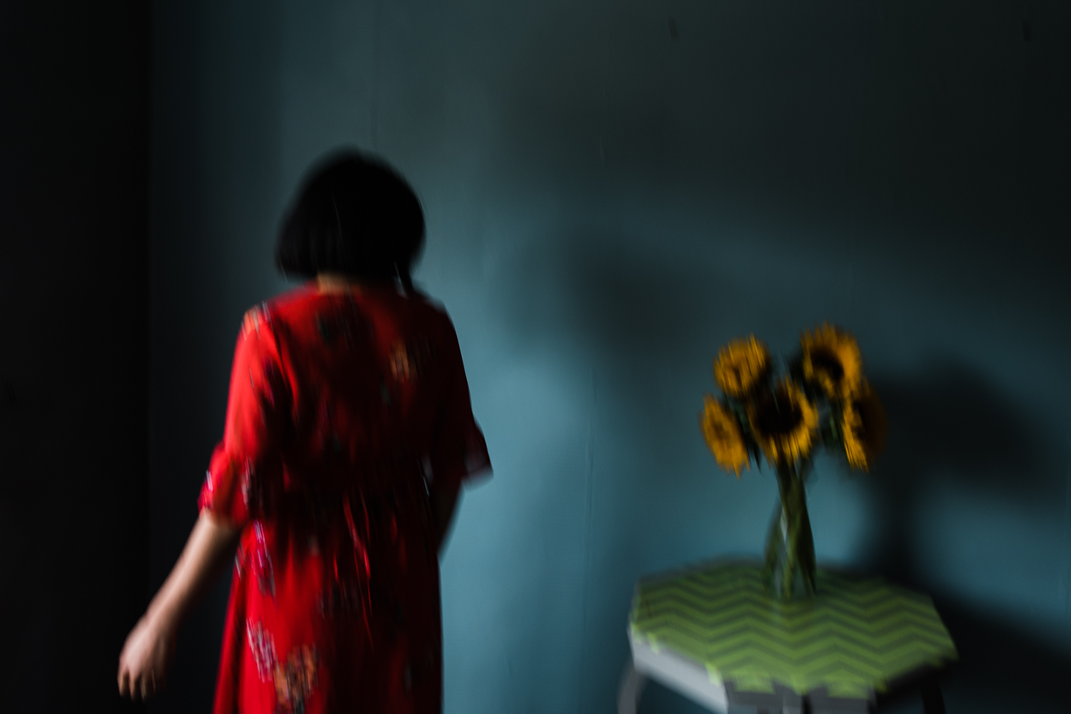 Artist stands by a green table with a vase of sunflowers on the