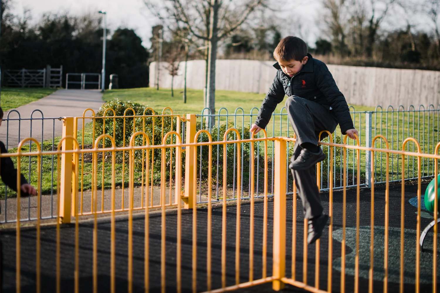 A boy climbs over a yellow railing in the playground