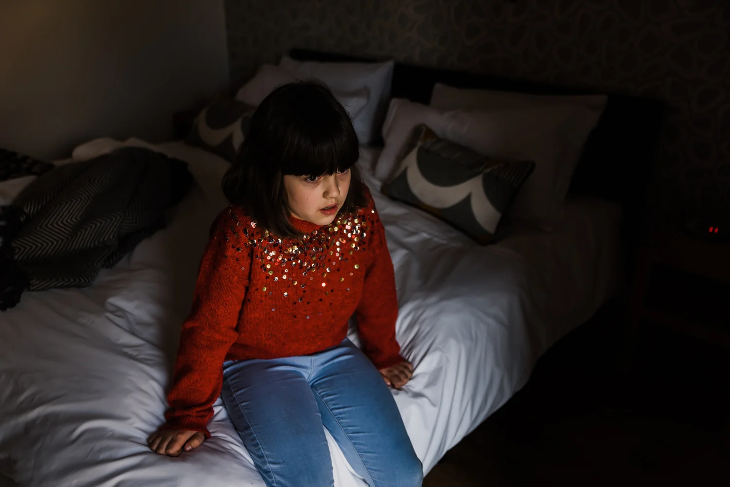 Girl in a red sequin jumper sitting on a bed in a child portrait