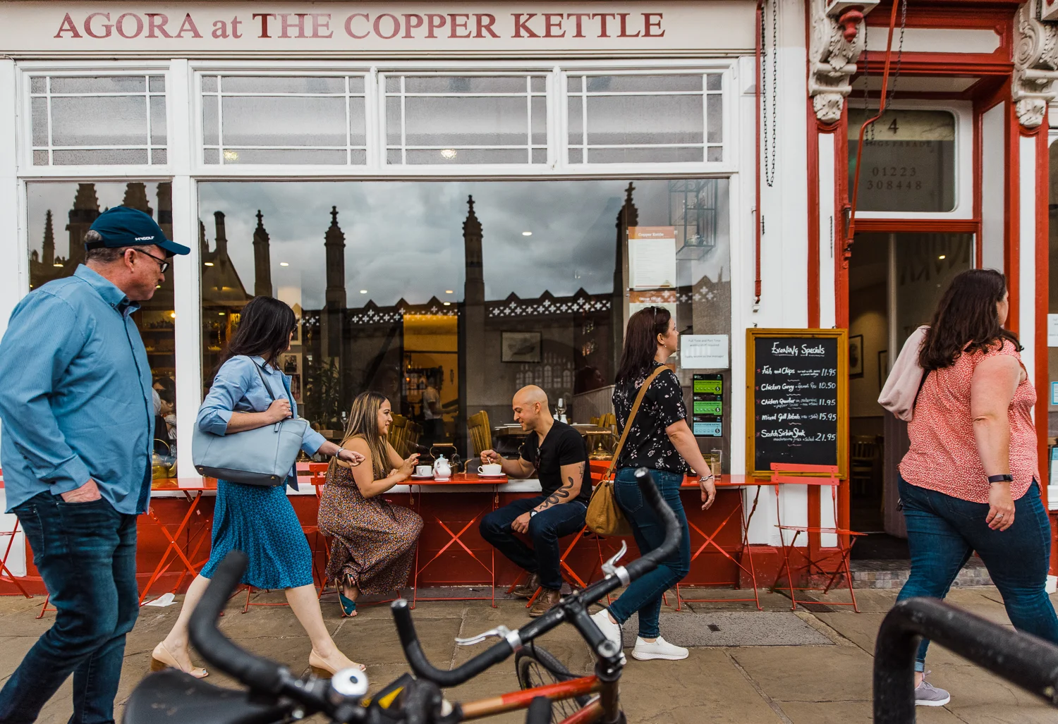 A couple sits outside drinking tea at The Copper Kettle in Cambridge as people walk by