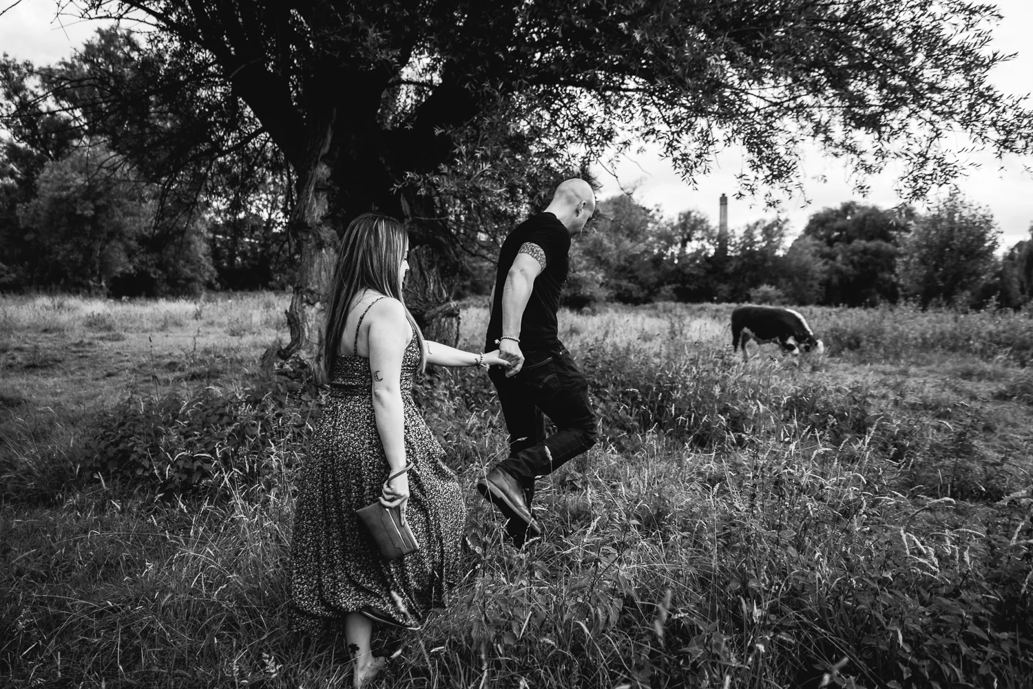 A man takes his girlfriend by the lead in the grassy meadow at Mill Pit, Cambridge