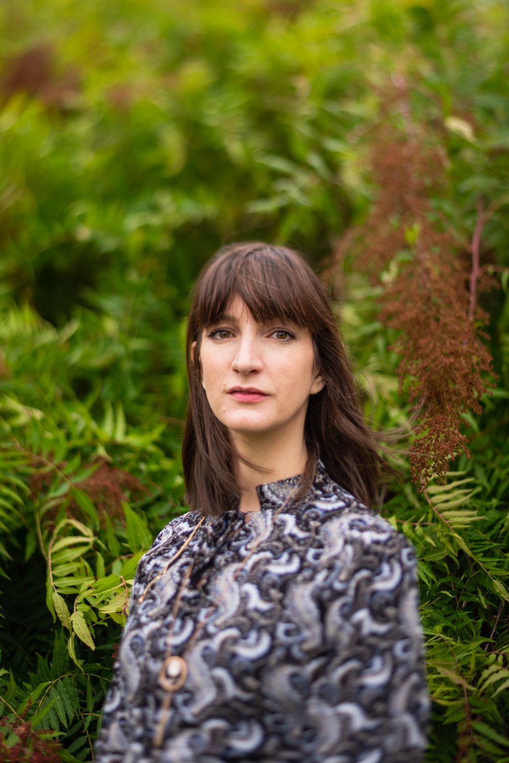  Soft-focus natural portrait of a female in a black paisley dress in front of a leafy background. 