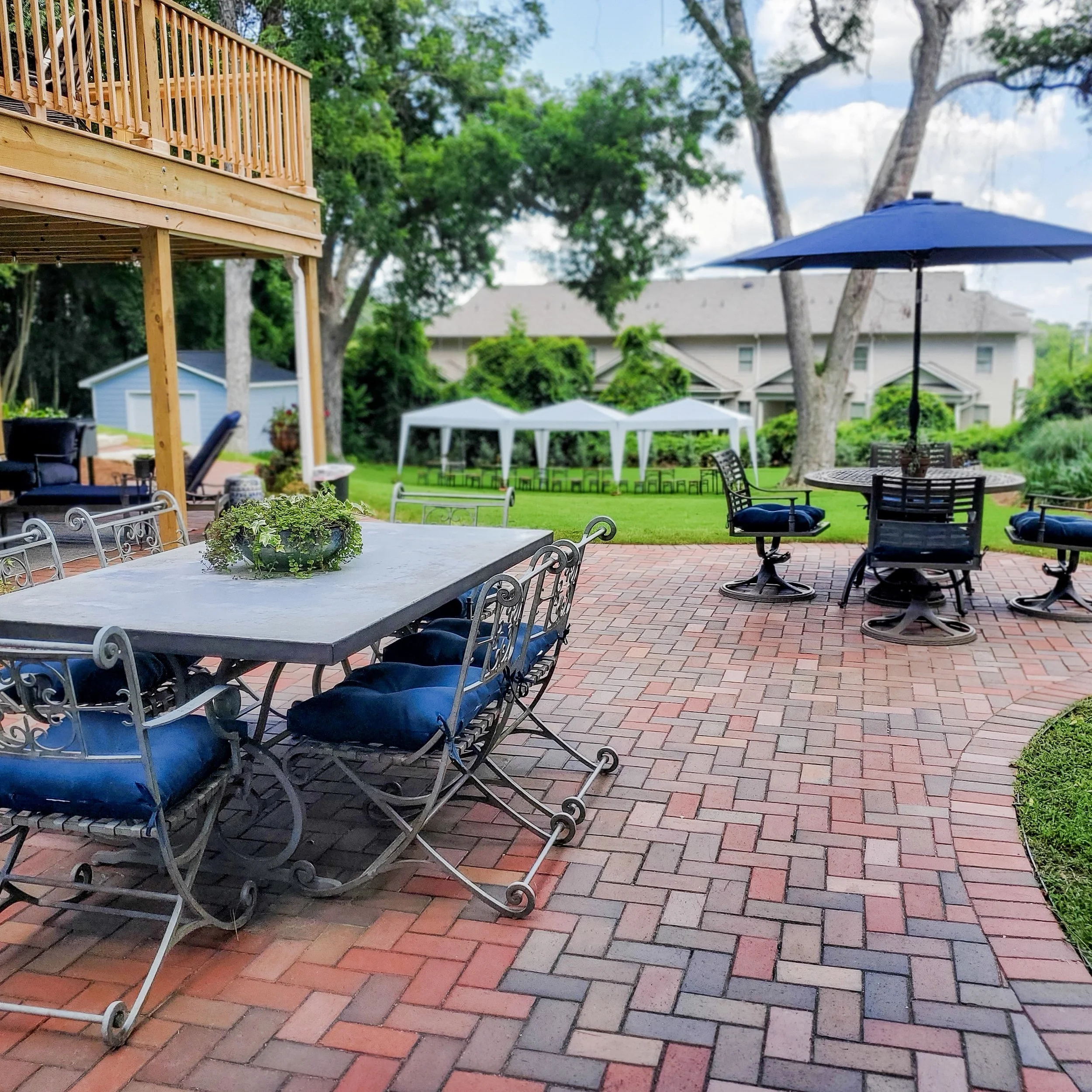 Outdoor patio area with tables, chairs, a large umbrella, and trees in the background.