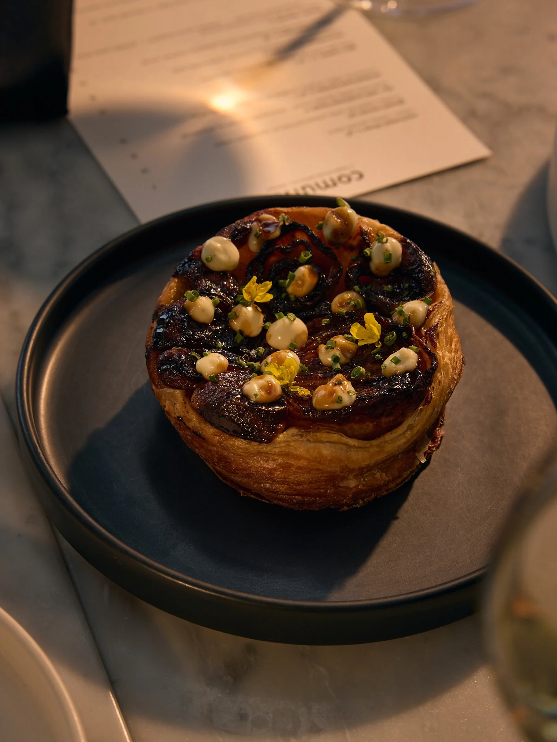 vegan tart tatins are hard to come by, and we&rsquo;ve got a sweet + savory version for this spring menu. flaky puff pastry gives this croissant crunch, topped with balsamic caramel roasted shallots and finished with a white truffle aioli + a drizzle