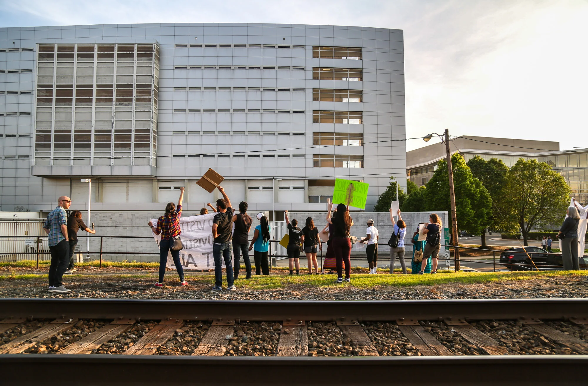 During the protest, people gather in front of the jail, some holding the signs, some writing slogans on the ground with chalks and some holding the speaker. They protest by singing and shouting and sometimes dancing. At the end of the protest, they march down both ends of the street and wave to people up in the bulding.