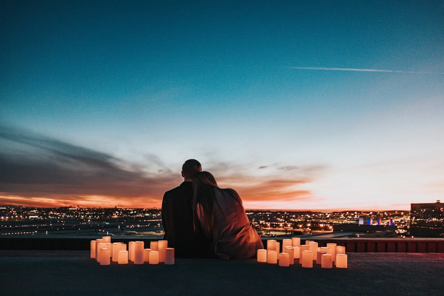 A photograph of a couple leaning against each other while looking at a city skyline at sunset