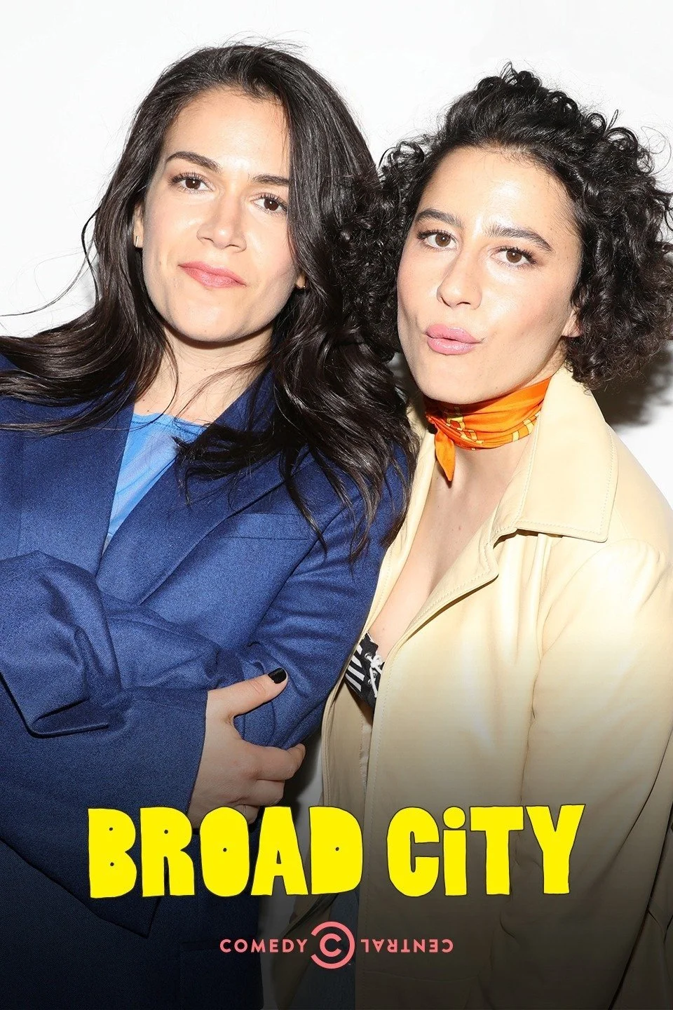 Two women posing together for a photo, one wearing a blue blazer and the other wearing a beige jacket with an orange scarf, with the words 'Broad City' and 'Comedy Central' at the bottom.